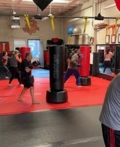Group of people practicing boxing with punching bags at The Dojo gym.
