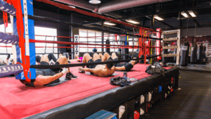 Boxers resting after training in a boxing gym with ring and equipment.