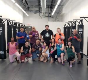 Group of diverse fighters in boxing gym with gloves and punching bags.