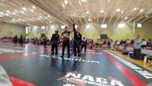 Two athletes celebrating victory on the grappling mat at a Brazilian Jiu-Jitsu event.