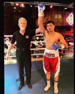 Young boxer with referee celebrating victory in boxing ring.