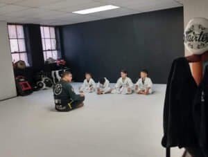 Kids practicing Jiu-Jitsu with instructor in a martial arts gym.