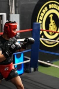 Boxer wearing red headgear and gloves training in boxing gym.