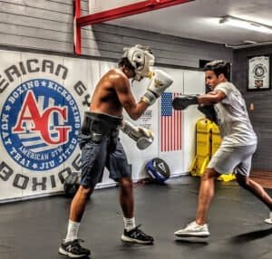 Two young men sparring in boxing gym with protective gear and gloves.