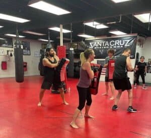People practicing cardio kickboxing with pads at Santa Cruz Boxing gym.