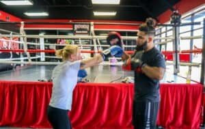 Female boxer practicing punch with trainer in boxing gym.
