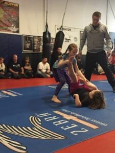 Young girls practicing Brazilian Jiu-Jitsu techniques in a training session.