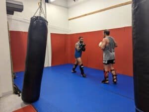 Two fighters practicing Muay Thai in a training gym with punching bags.