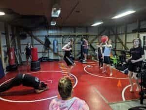 Group of fighters training with boxing gloves and punching bags in gym.