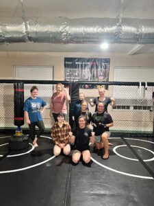Group of women training in MMA gym with cage and boxing equipment.