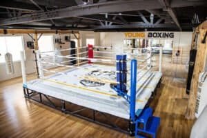 Indoor boxing training ring in a modern gym with wooden floors and bright lighting.