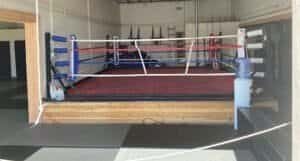 Indoor boxing ring with red mat and blue corner pads at Blackout MMA.