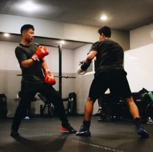 Two men practicing boxing in a gym with focus mitts and gloves.