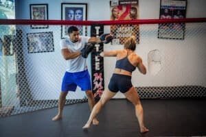 Female fighter practicing striking with male trainer in MMA gym.