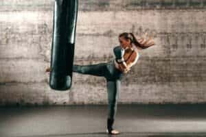 Female athlete practicing kickboxing with punching bag in gym.