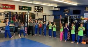 Children practicing martial arts in a gym with boxing equipment.