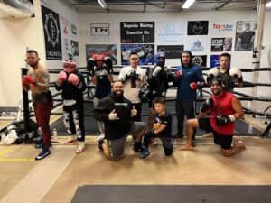 Group of boxers and trainers in boxing gym with gloves and gear.
