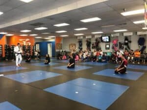 Students practicing martial arts in a dojo with instructor and spectators.