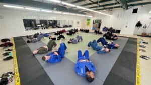 Students practicing Brazilian Jiu Jitsu techniques on mats in a training facility.