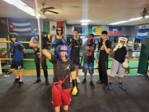 Young kids practicing boxing in a gym with boxing gear and flags in the background.