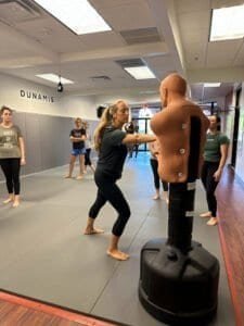 Woman practicing striking techniques on a punching dummy in MMA class.