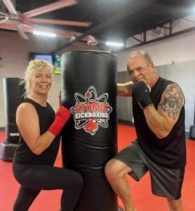 Two people training with a punching bag at Atomic Kickboxing gym.