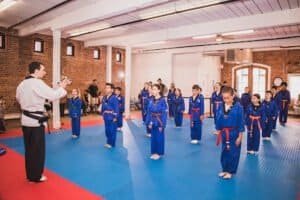Children in blue martial arts uniforms practicing under instructor supervision.