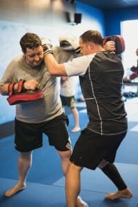 Two men practicing boxing techniques in a gym with focus mitts and gloves.