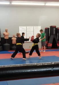 Children practicing martial arts with pads in a gym at Success Martial Arts.