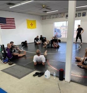 Students practicing Brazilian Jiu-Jitsu techniques on mats in a training class.