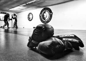 Boxing gloves placed on the floor in a gym with fighters training in the background.