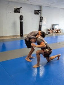 Two practitioners practicing Jiu Jitsu techniques on blue mats.