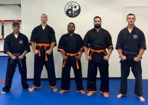 Group of martial artists in black uniforms with colored belts at Empire Defense & Fitness.