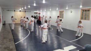 Children practicing martial arts in a dojo with orange belts and white uniforms.
