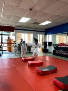 Children practicing martial arts in a dojo with pads and instructors.