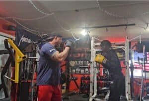 Two men boxing training in Mc1fitness gym with punching bags and equipment.