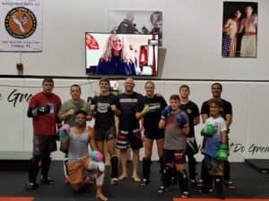 Group of fighters and trainers in MMA gym with boxing gloves and gear.