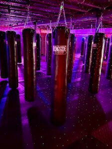 Indoor boxing gym with punching bags and purple lighting for training.