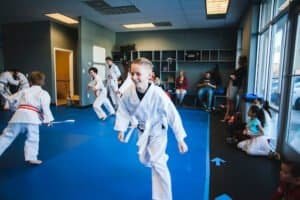 Children practicing martial arts in a dojo with instructor and parents watching.