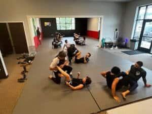 Students practicing Brazilian Jiu Jitsu techniques on mats in a training room.