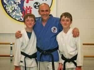 Martial arts instructor with two young students in gi uniforms.