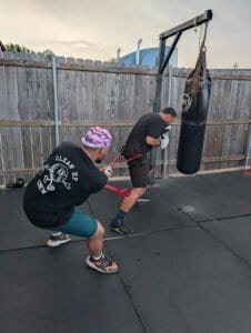 Two men practicing boxing techniques with a punching bag outdoors.