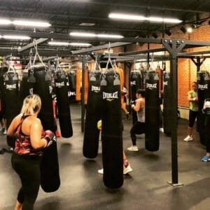 Boxing gym with hanging punching bags and people training.