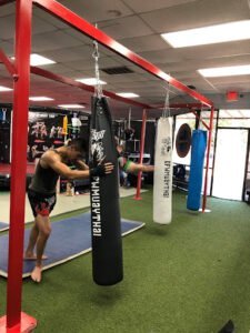 Young boxer practicing punches on heavy bag at Muay Thai gym.