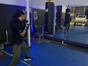 Female boxer practicing punches in boxing gym with punching bags.