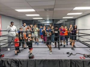 Group of children and teens training boxing in a gym with boxing ring.