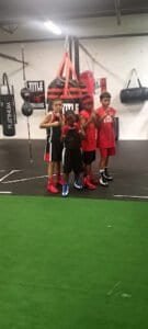 Young boys practicing boxing in gym with punching bags and training gear.