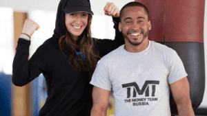 Female boxing coach and male athlete smiling after training session.