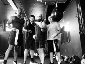 Group of diverse boxers and trainer in gym with punching bag.