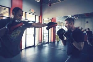 Two men sparring in boxing gym with punching bags and mirrors.